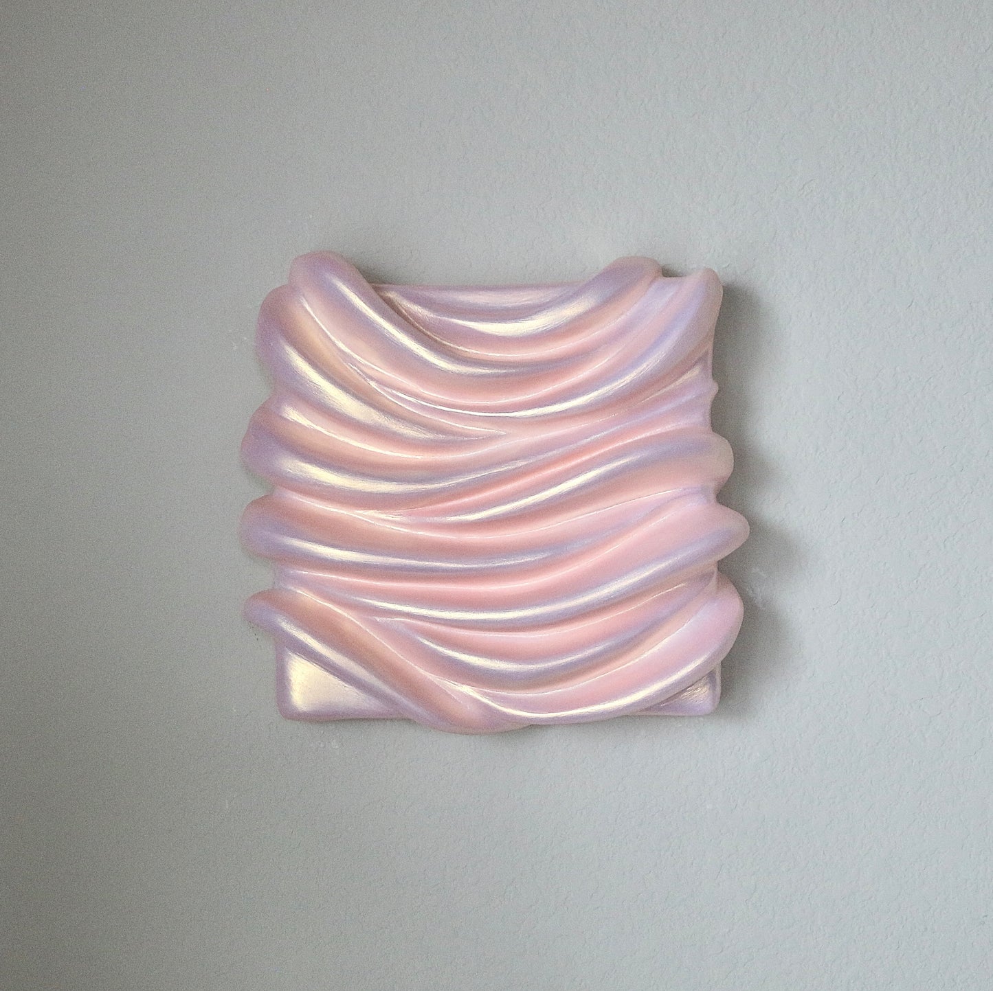A sculpture artwork represented as a abstract, amorphous form with a smooth, possibly metallic surface in an pinkish hue, mounted on a wall.