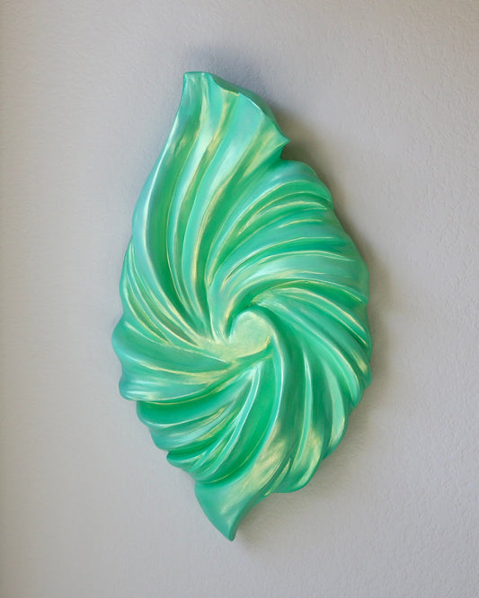 Decorative green and white wall art on a plain wall next to a window.