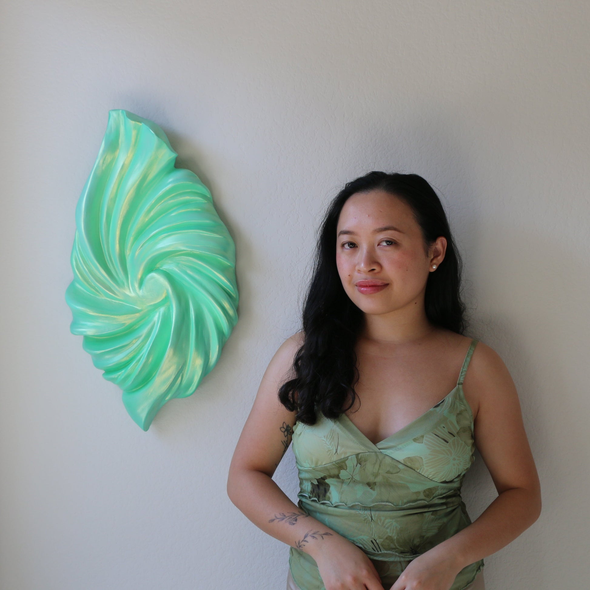 Woman in a green dress standing next to a decorative wall piece in a room.