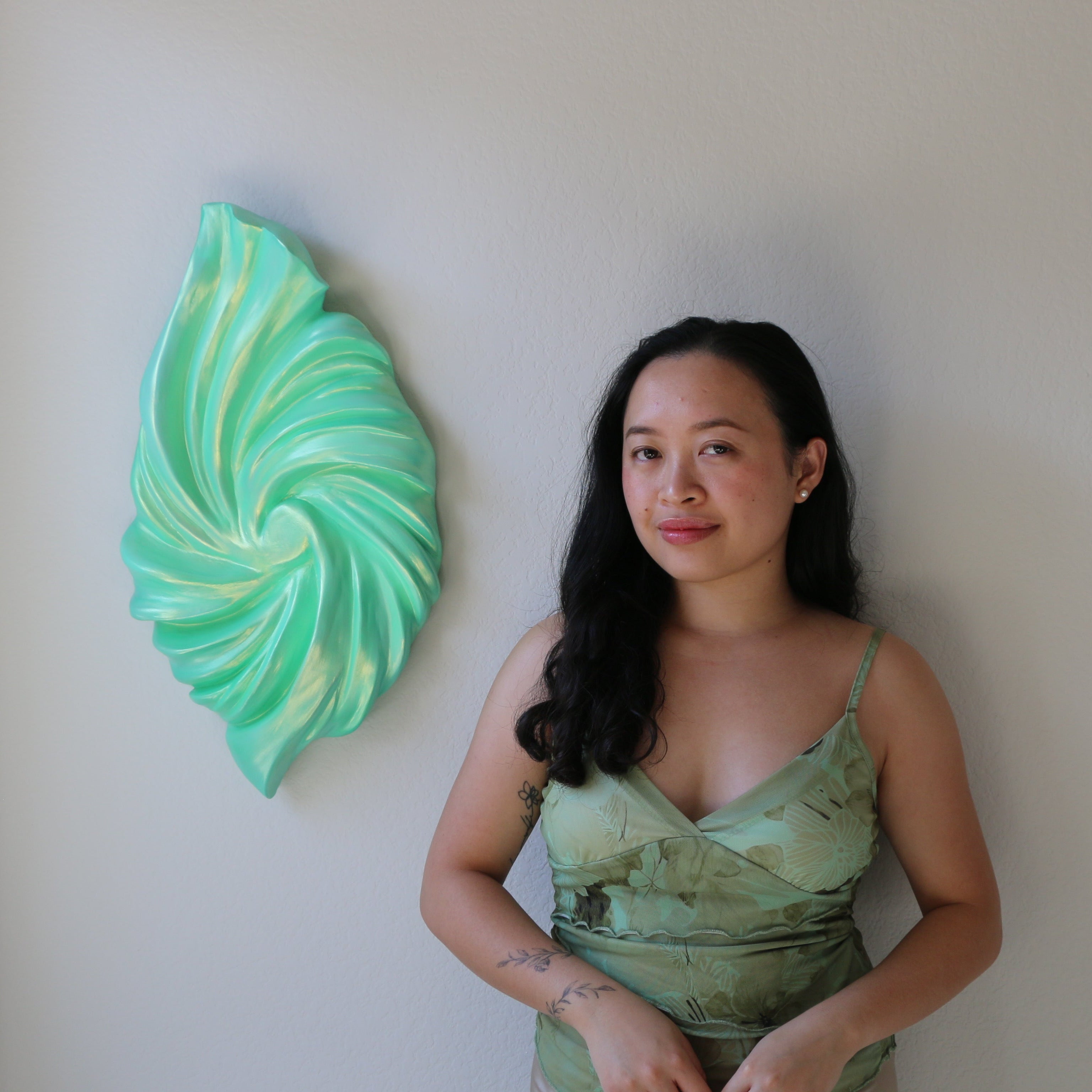 Woman in a green dress standing next to a decorative wall piece in a room.